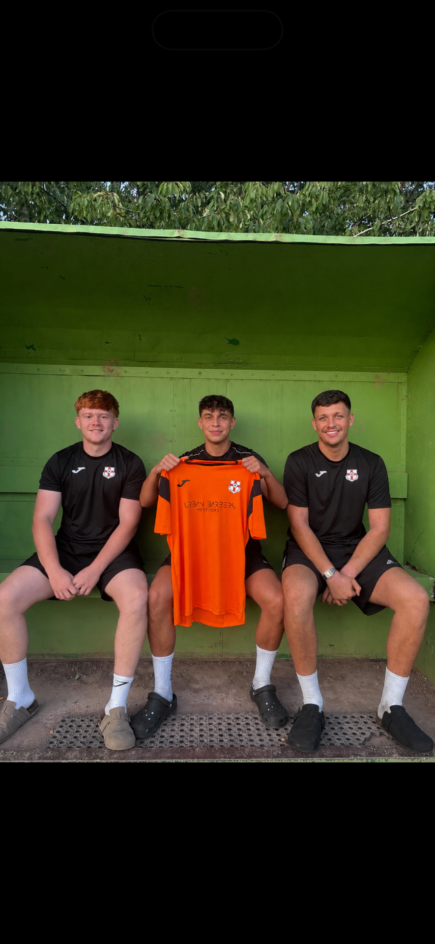 Jude Cook holding up the Burghill Rangers 26/27 home shirt alongside teammates